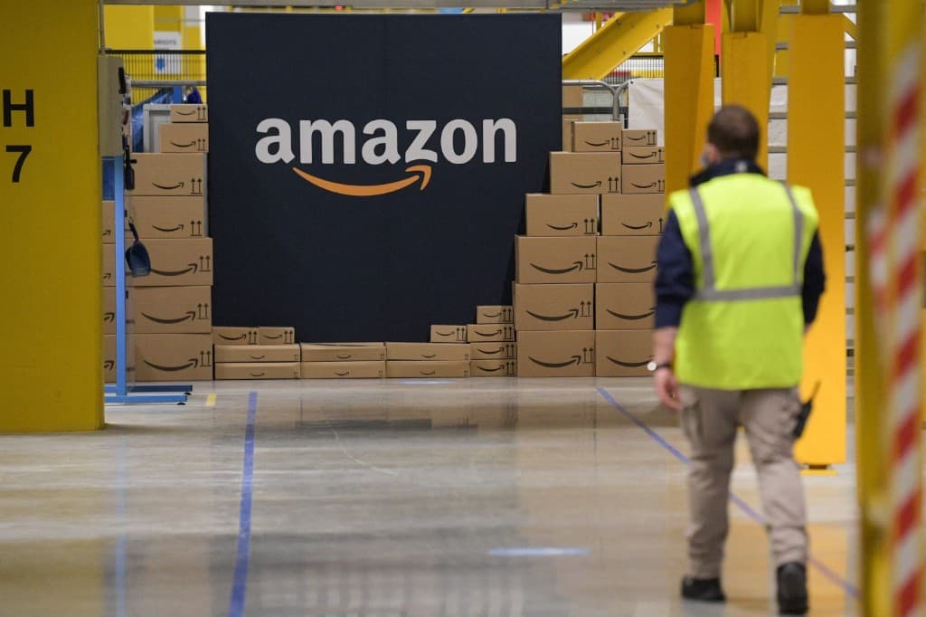 Stacked Amazon shipping boxes beside the Amazon logo wall